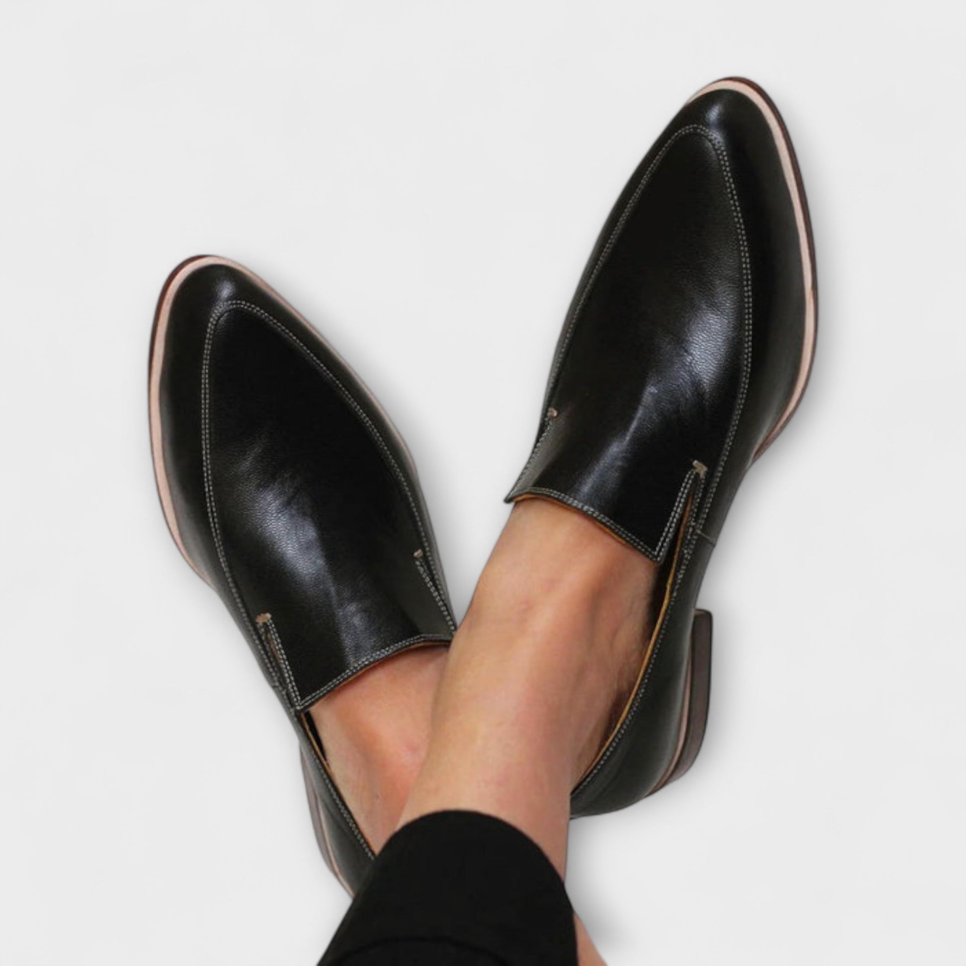 Black leather slip-on loafers with contrast stitching and tan sole, worn on feet