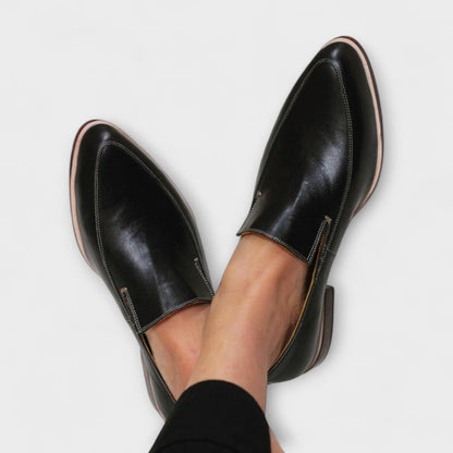 Black leather slip-on loafers with contrast stitching and tan sole, worn on feet
