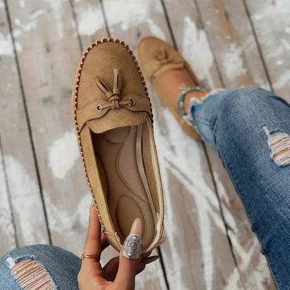 Tan suede bow loafer held in hand showing cushioned insole detail