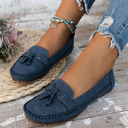 Navy suede loafer with bow detail and cushioned sole, worn on wooden surface