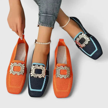 Navy and orange knit loafers with gold square buckles styled on feet with jeans