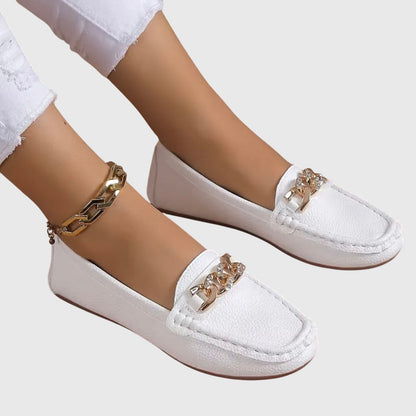 White textured loafers with rose gold chain link trim worn on feet