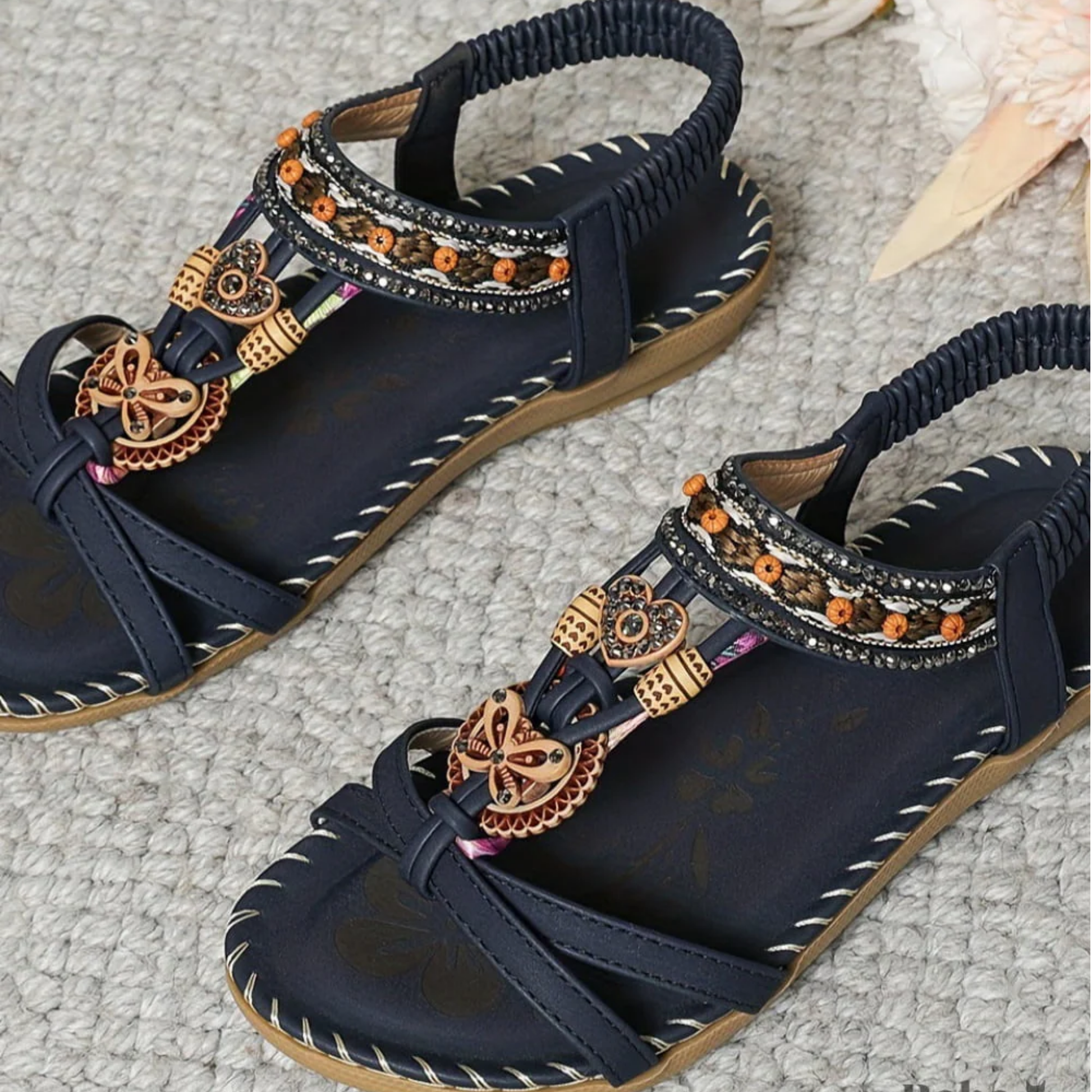 Black t-strap sandals with decorative beaded charms and patterned ankle straps from above