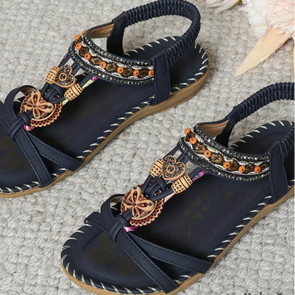 Black t-strap sandals with decorative beaded charms and patterned ankle straps from above