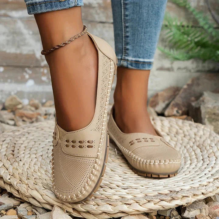Cream perforated moc toe loafer flats with decorative stitching on wearer's feet