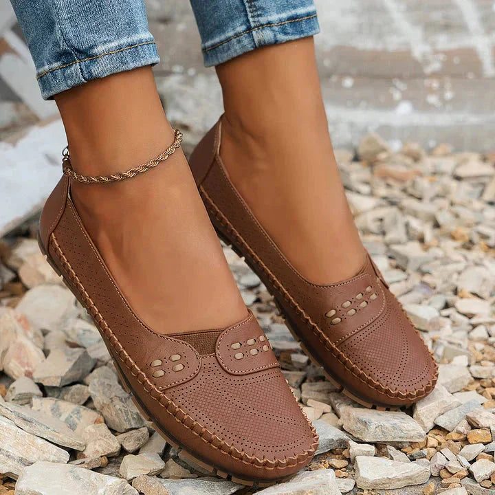 Brown perforated moc toe loafer flats with stud embellishment worn casually