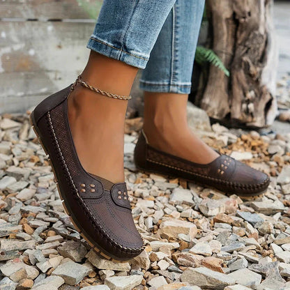 Dark brown loafer flat with arch support worn on gravel showing textured upper and comfort sole