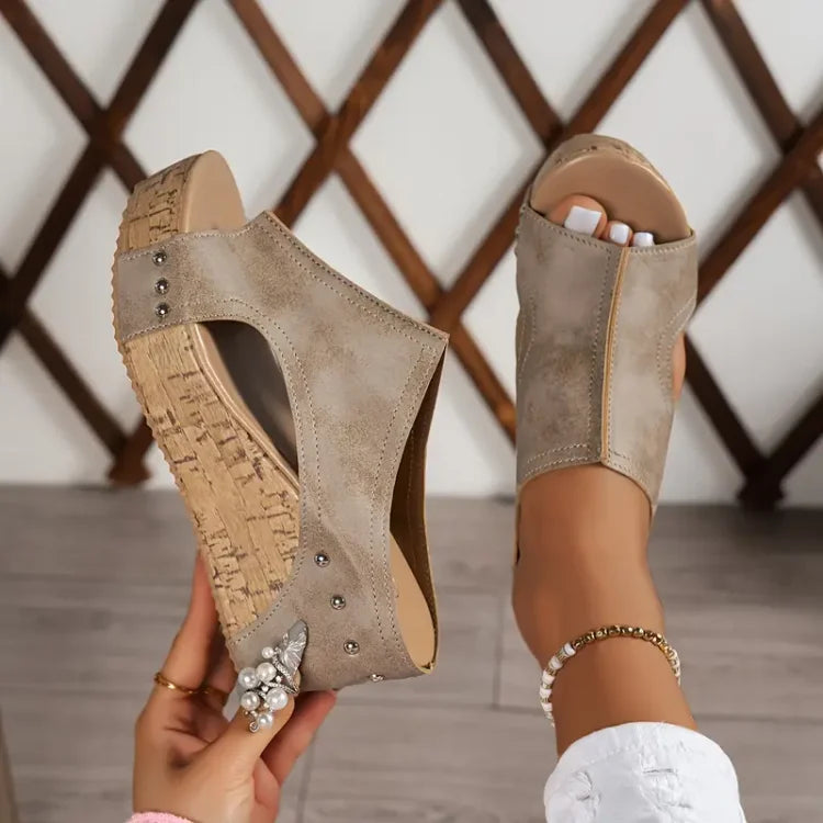 Beige suede studded cork wedge sandals held in hand showing sole detail